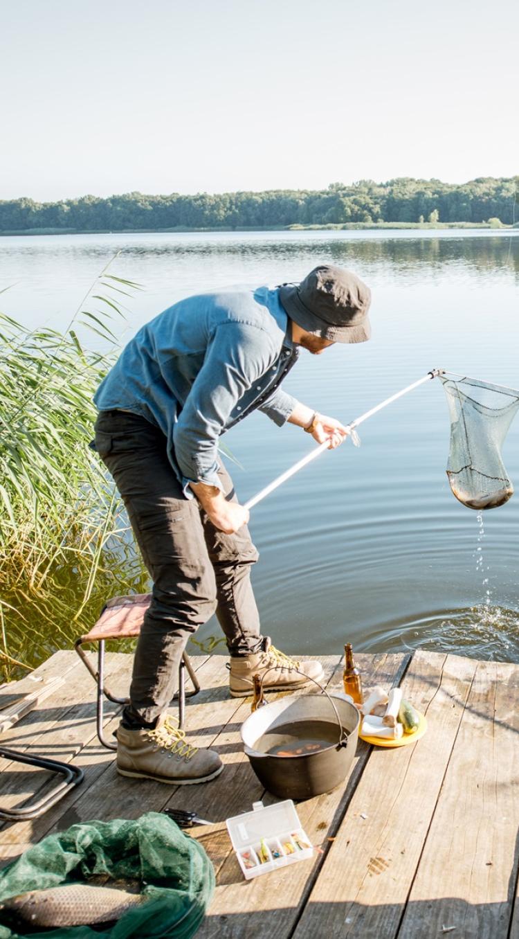 Twee mannen aan het vissen in Limburg vanaf een houten steiger aan een rustige visvijver, omringd door riet en bos.