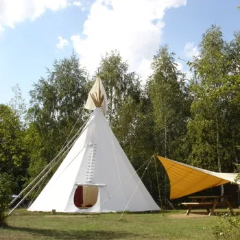 Witte tipi op een open grasveld bij Natuurkampeerterrein Wega in Weert, omgeven door bomen en voorzien van schaduwdoek en picknicktafel.