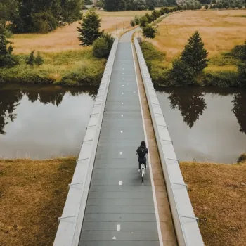 Een fietser rijdt over een strak aangelegd fietspad boven de Roer, omgeven door graslanden en bomen in het Limburgse landschap.