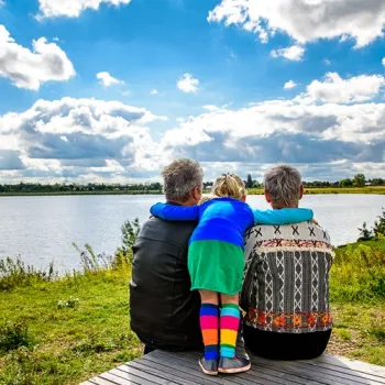 Drie personen zitten op een bankje aan de Maasplassen en kijken uit over het water en het groene landschap.